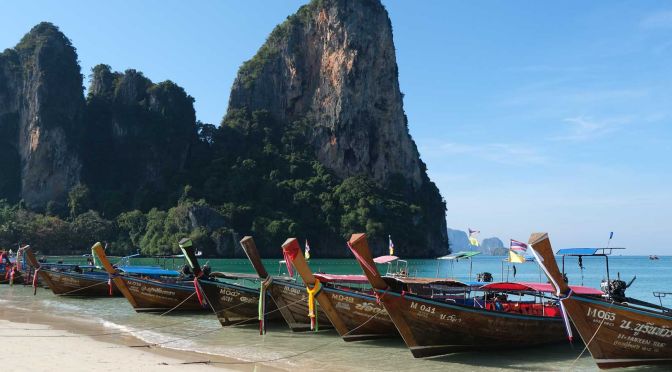 Shows an image of long tail boats lined up in Railay Beach, Krabi - Visiting Thailand in January