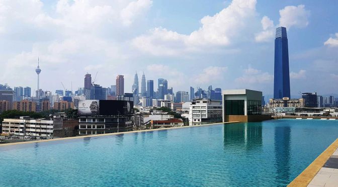 Shows a swimming pool and the Kuala Lumpur skyline